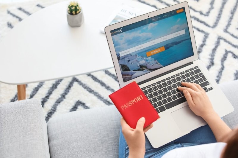 Frau hält einen Reisepass und bucht einen Flug am Laptop.