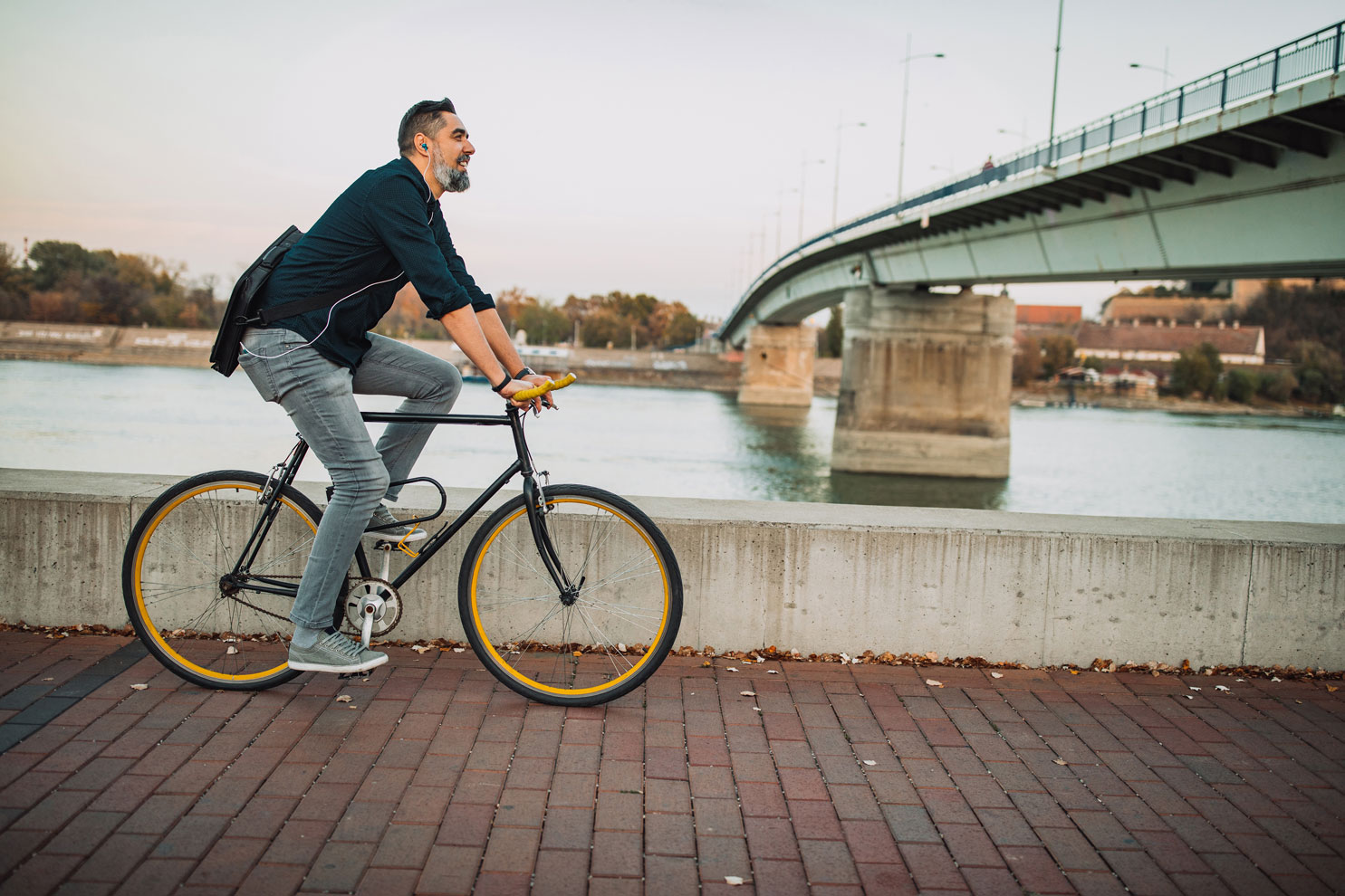 Fahrradfahrer mit Kopfhörer und Aktentasche fährt an einem Fluss entlang.