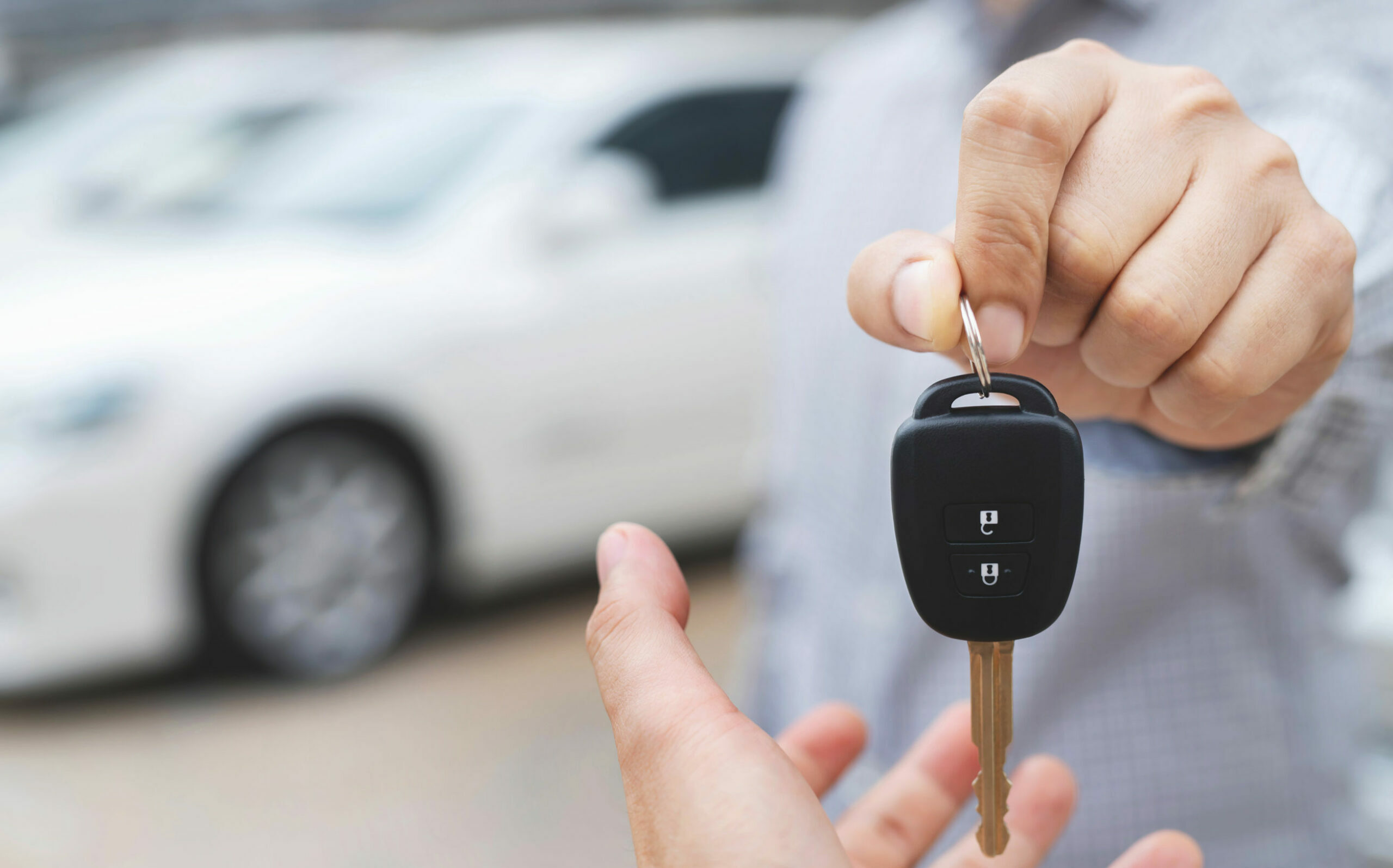 Une main met une clé de voiture dans la paume d'une autre main avec une voiture en fond