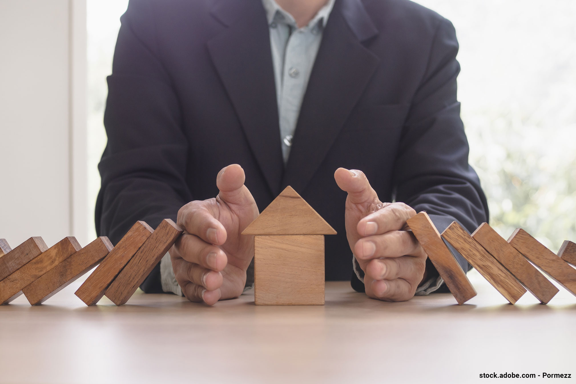 Représentation du rôle d'une assurance habitation avec des mains qui protègent une maison miniature menacée