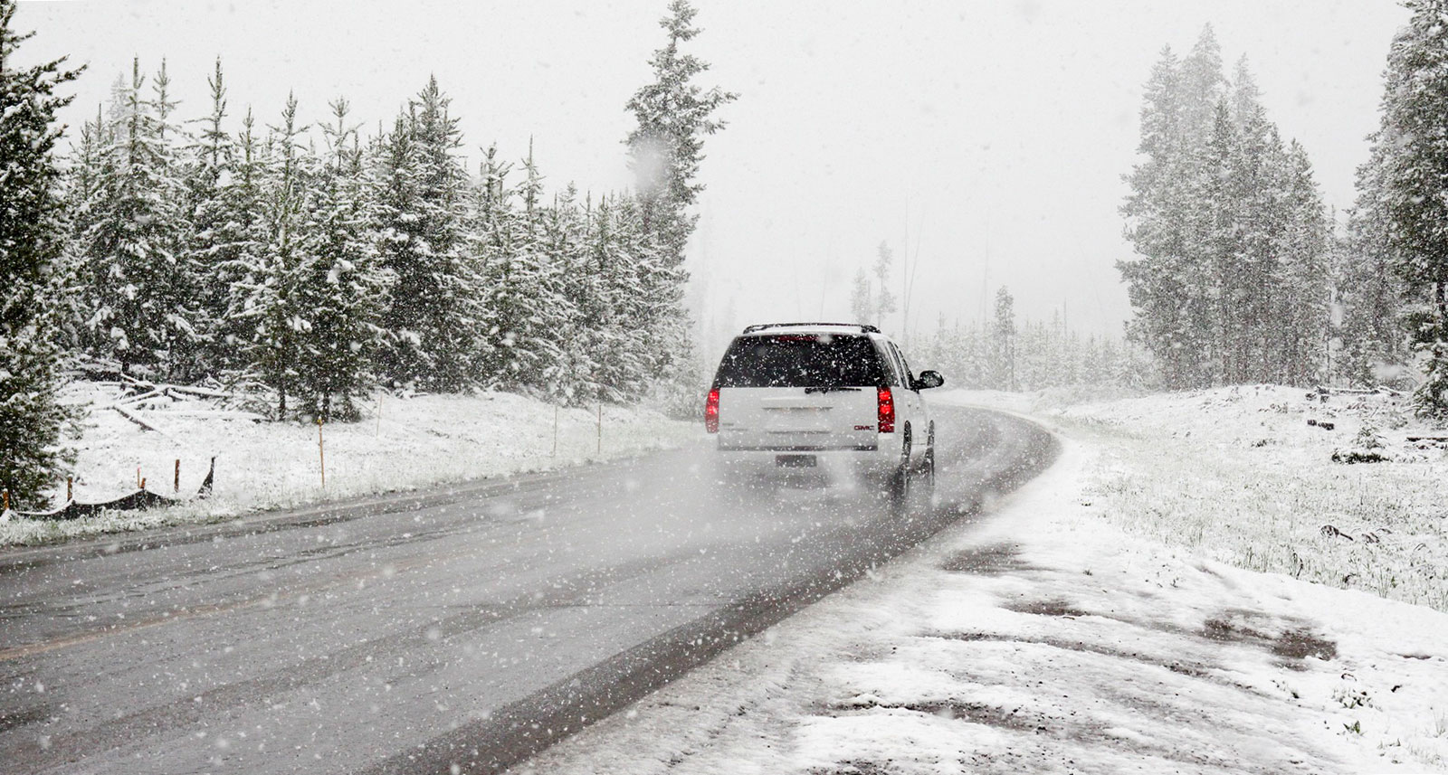 Une voiture blanche circule sur une route entourée de neige