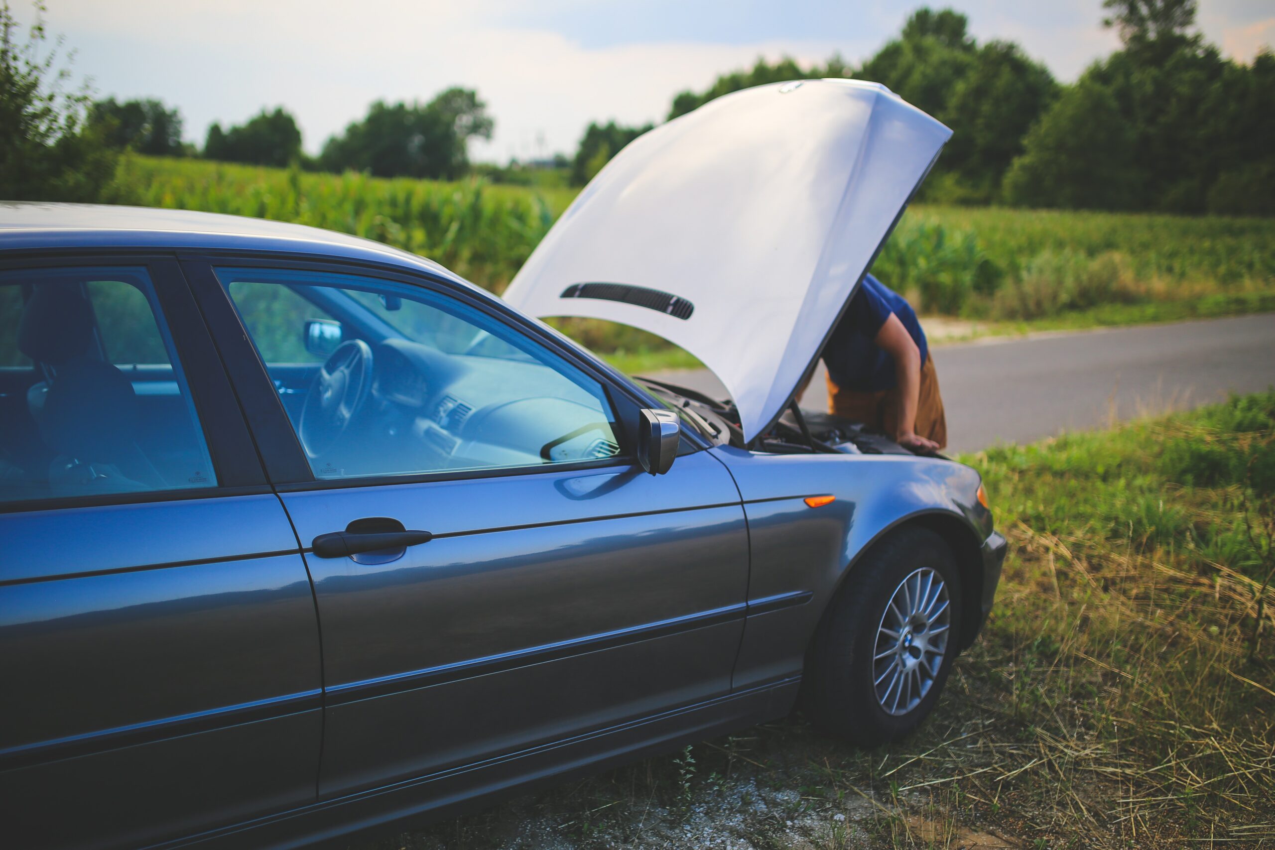 Une voiture est arrêtée au bord d'une route avec le capot ouvert et une personne qui regarde ce qui ne fonctionne pas