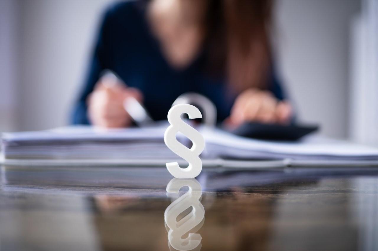 Frau am Schreibtisch, davor Paragraph.