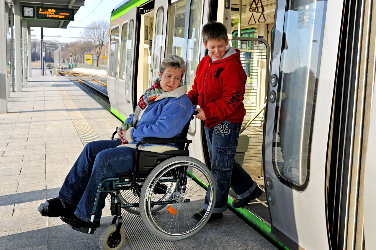 Une personne en situation de handicap avec un jeune enfant qui l'aide à monter ou à descendre d'un tram