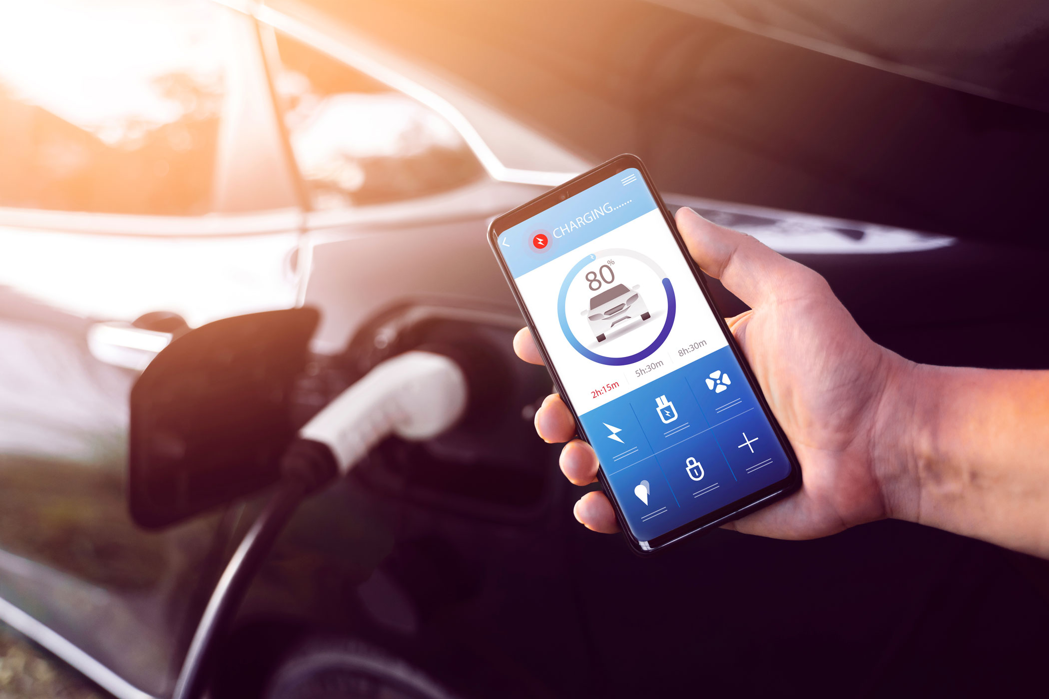 Personne tient un smartphone sur lequel fonctionne une application pour suivre la recharge sur une borne d'un véhicule électrique