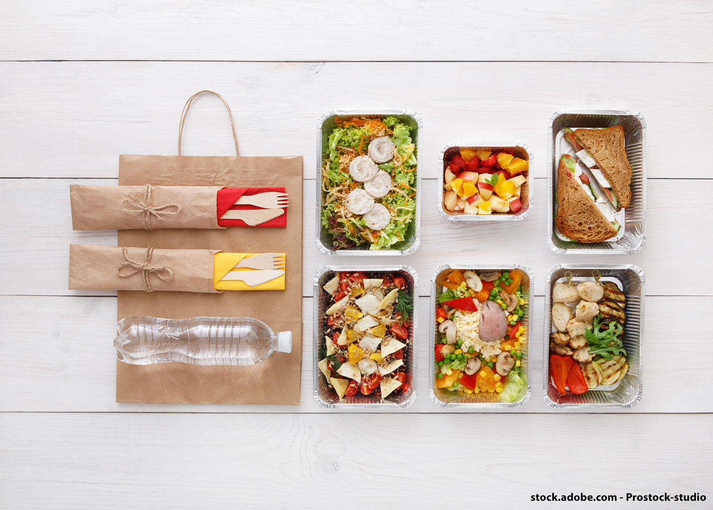 Des plats à emporter, servis dans des contenants en aluminium sont disposés sur une tables à côtés de couverts en carton et non en plastique