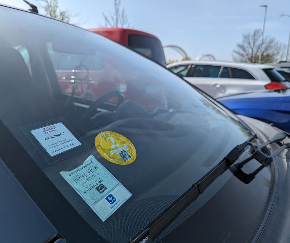 Sur le pare-brise de cette voiture, il y a trois macarons dont la carte verte d'assurance automobile