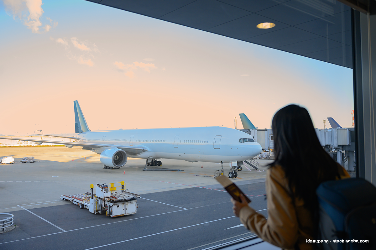 Une femme regarde un avion par la vitre de l'aéroport, un sac à dos sur le dos et son passeport en main