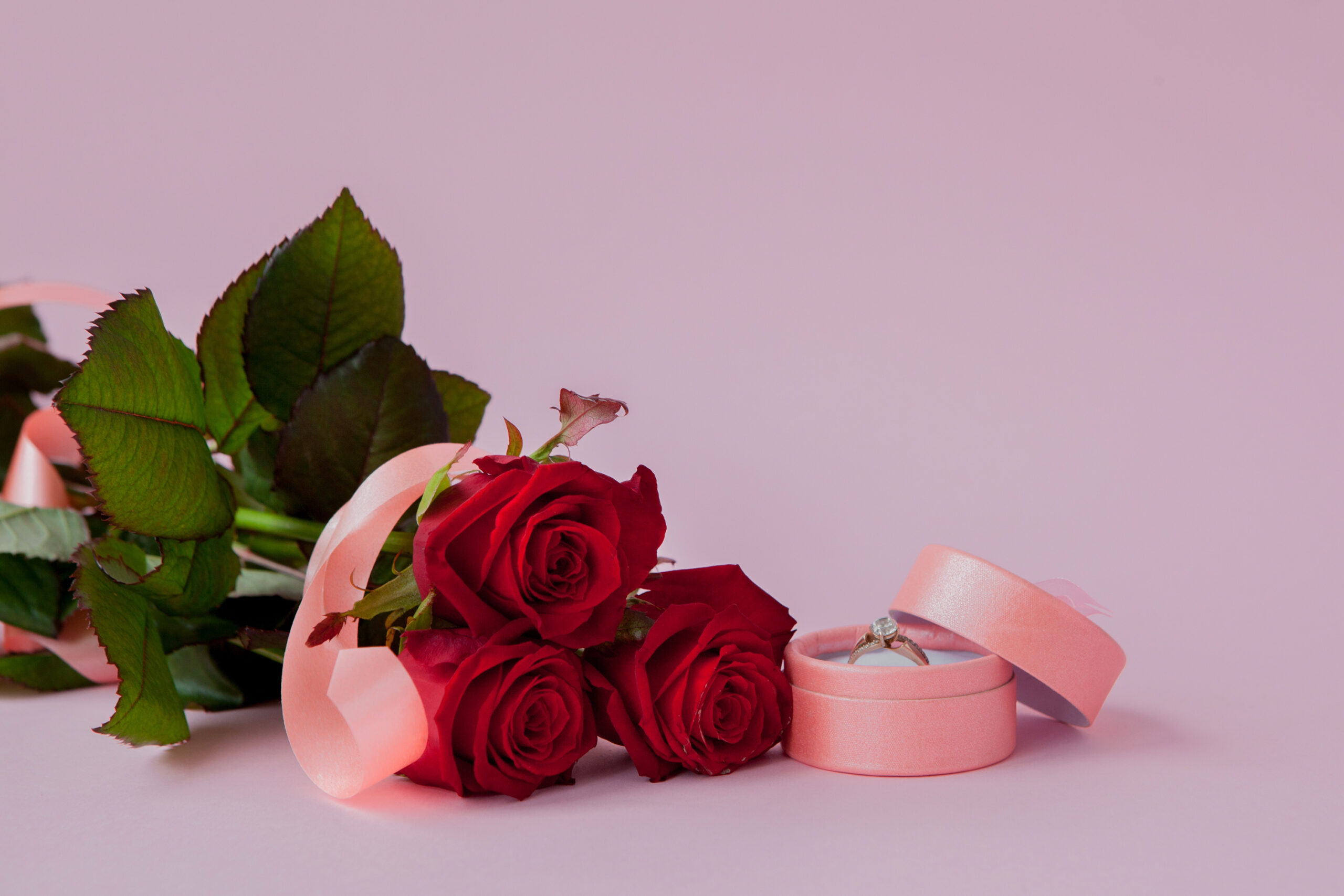 Wedding rings and wedding bouquet of red roses on wooden table, horizontally Selective focus, the background is blurred.