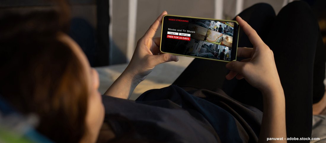 Une personne allongée sur un lit qui consulte un site de streaming sur son téléphone