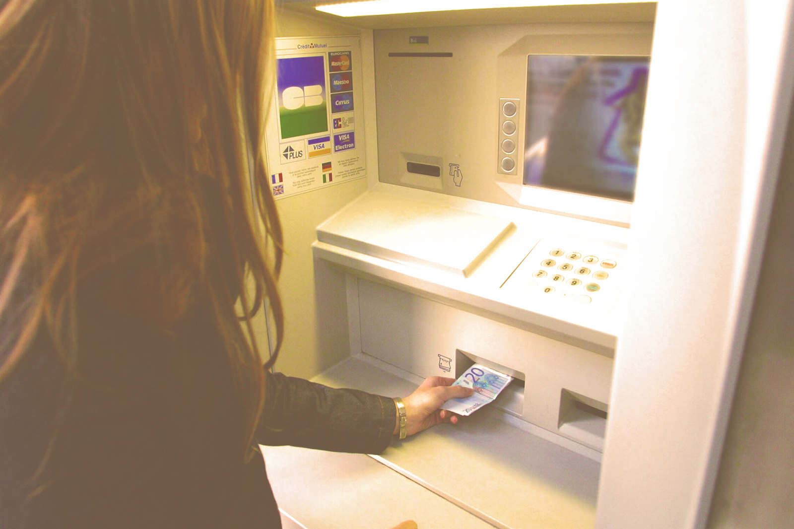 Une femme retire un billet de 20 euros à un distributeur automatique.