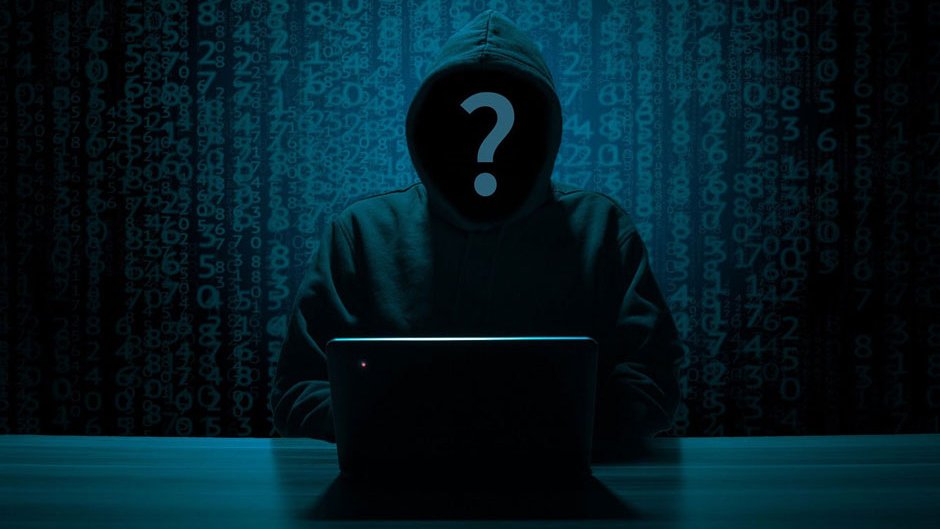 A hacker sits in a dark room in front of his laptop.
