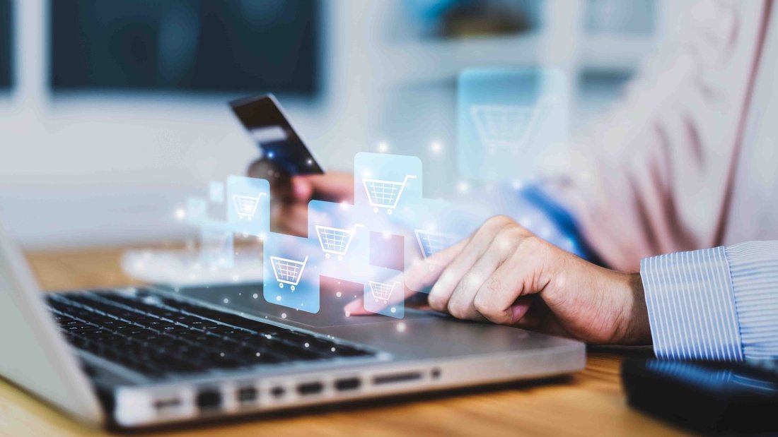 Eine Person hat ihre Hände auf einer Laptop-Tastatur, auf der stilisierte Einkaufswagen abgebildet sind.