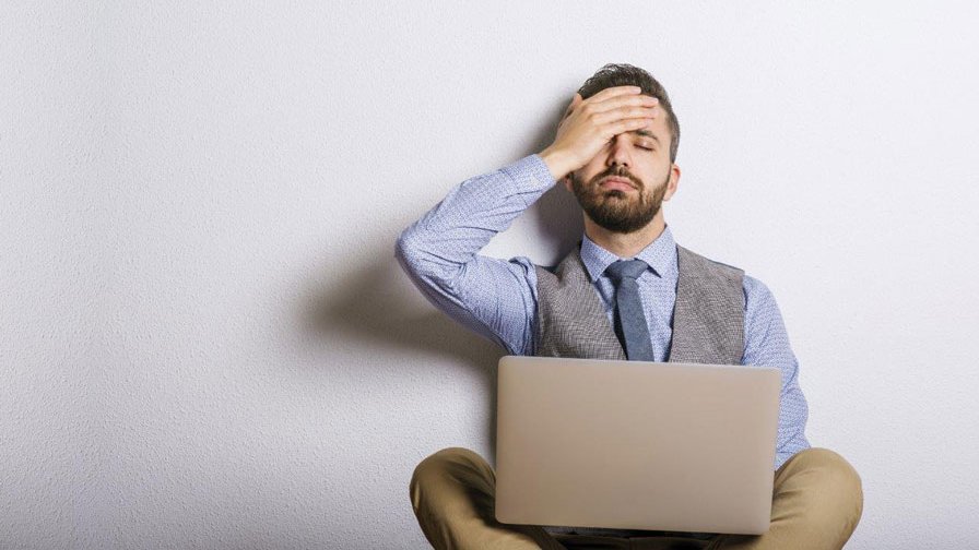 Ein Mann sitzt vor seinem Laptop und hält beschämt sich die Hand an den Kopf.