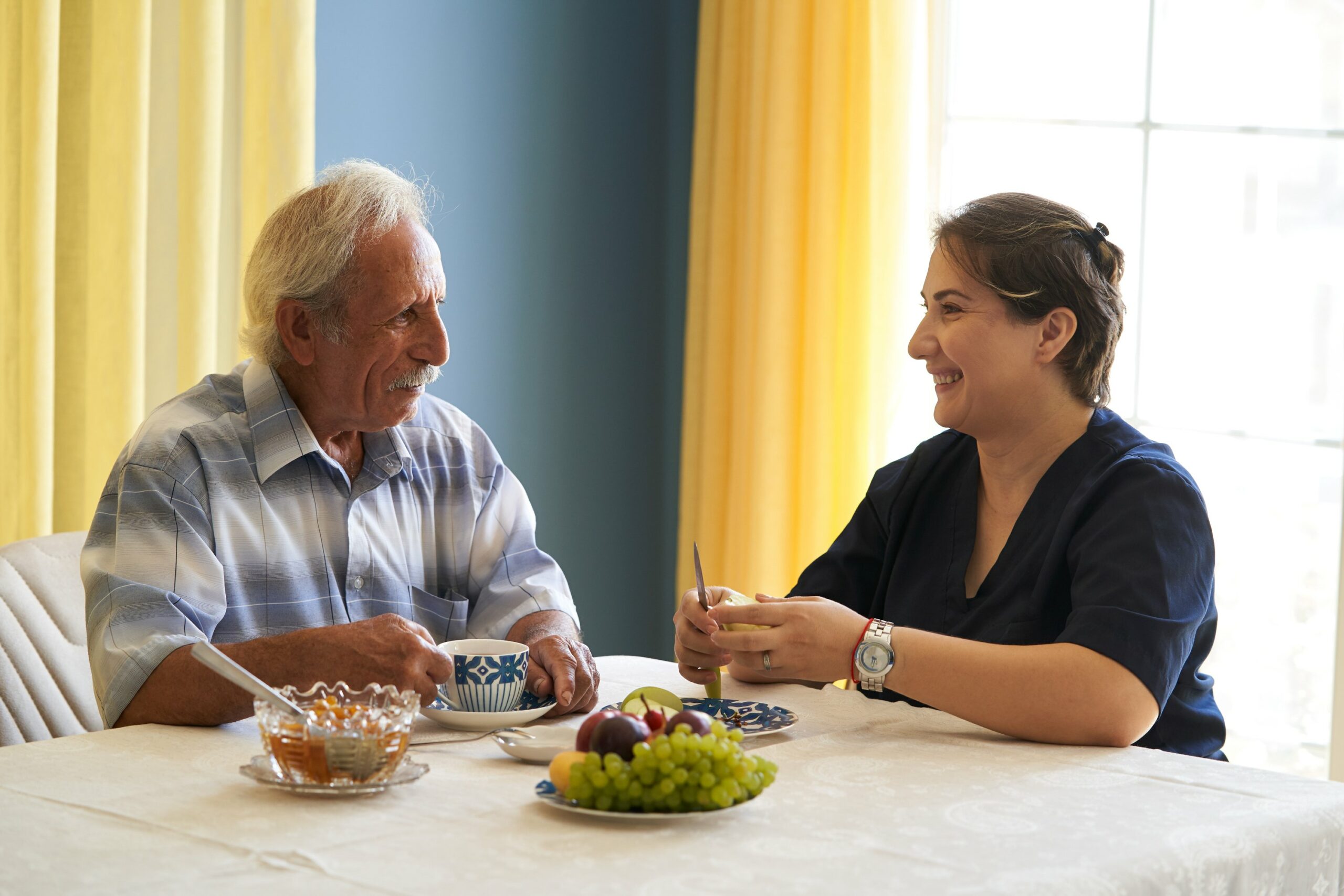 Ein älterer Herr sitzt mit der Pflegekraft beim Frühstück.