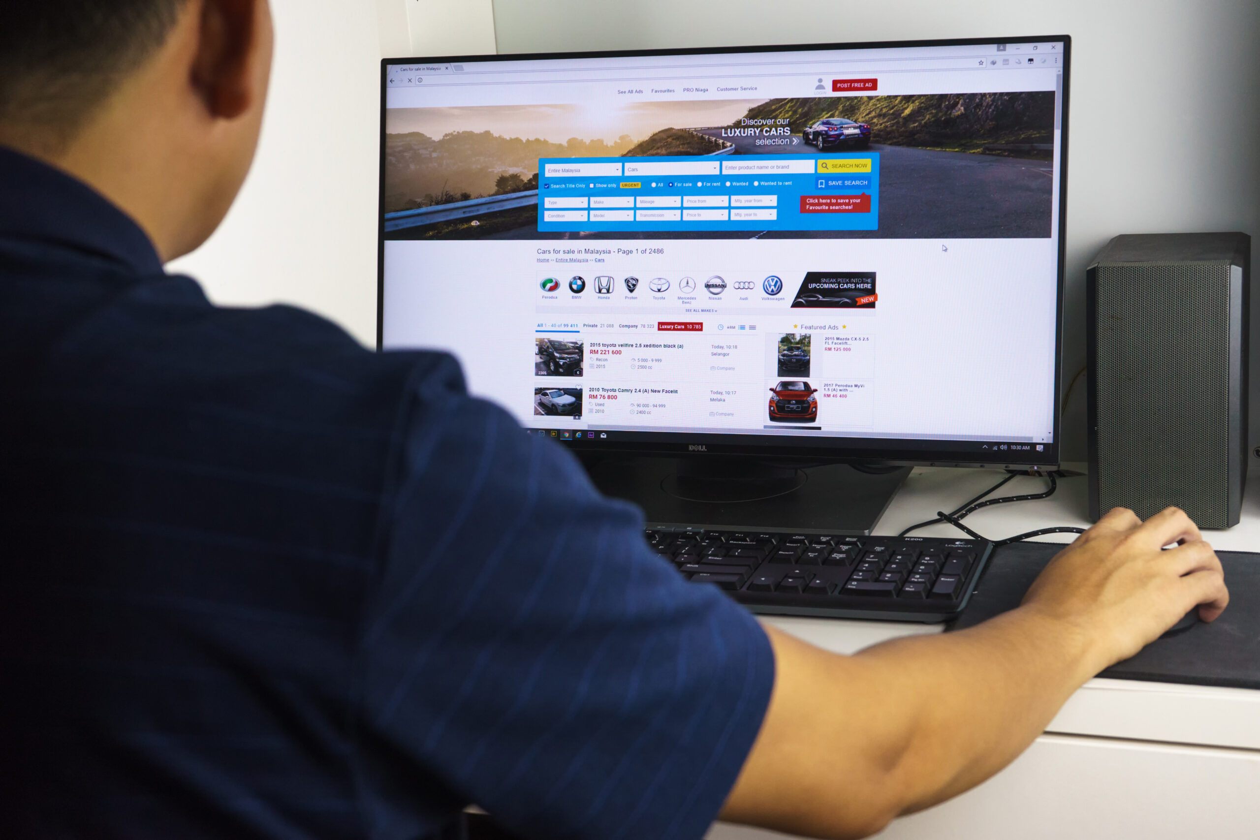 Ein Mann sitzt am Schreibtisch und sucht auf einem Online-Portal ein Auto zum Kauf.